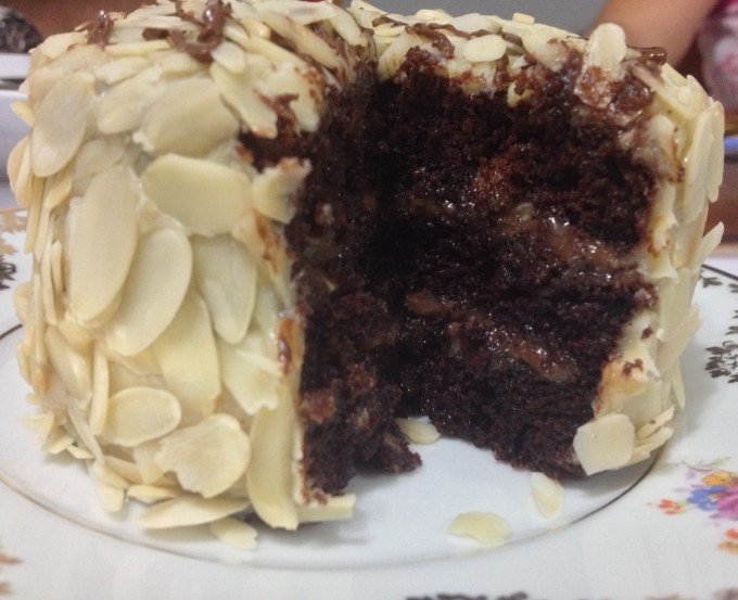[Bolo fofinho, sabor intenso de chocolate e bem recheado com creme de avelã e a cobertura com creme de leite condensado e lâminas finas e crocantes de amêndoas]