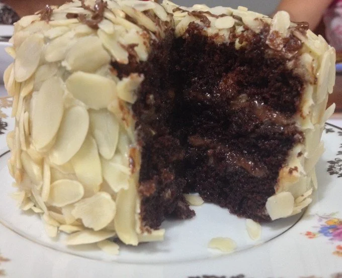 [Bolo fofinho, sabor intenso de chocolate e bem recheado com creme de avelã e a cobertura com creme de leite condensado e lâminas finas e crocantes de amêndoas]